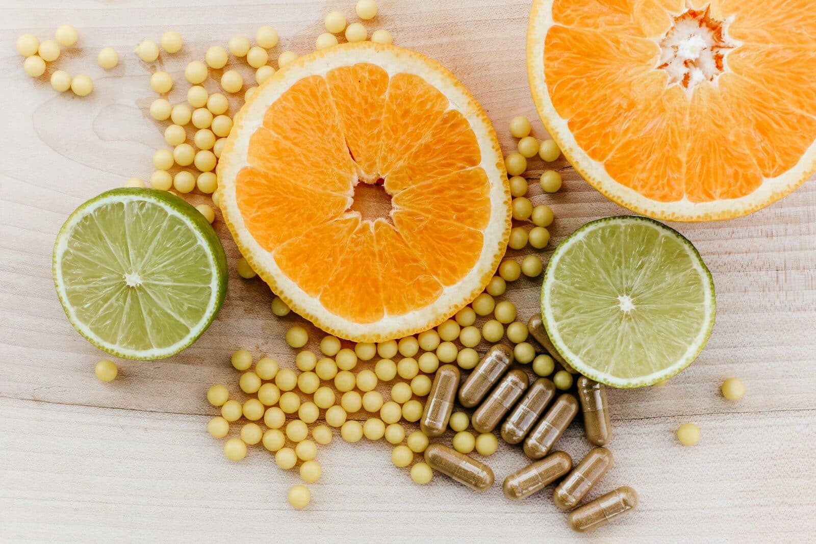 Citrus slices, small yellow supplement beads, and brown capsules on a wooden surface